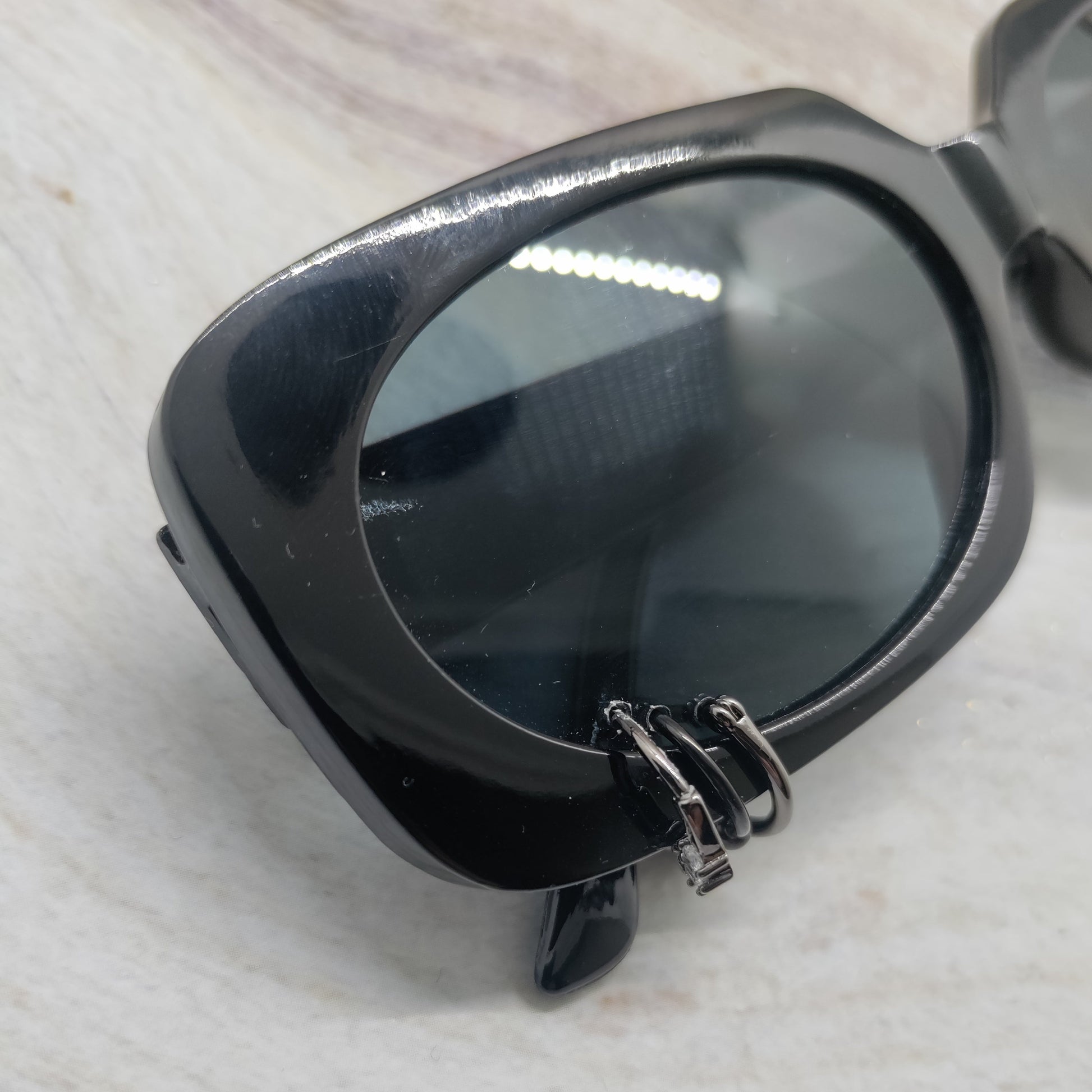 Black sunglasses with a glossy frame and dark tinted lenses, resting on a light textured surface.