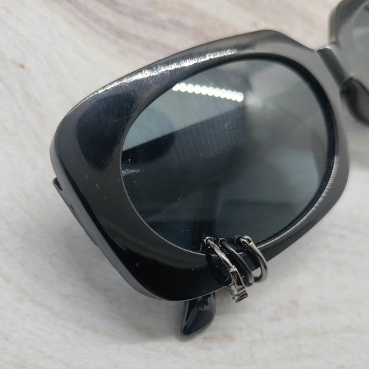 Black sunglasses with a glossy frame and dark tinted lenses, resting on a light textured surface.