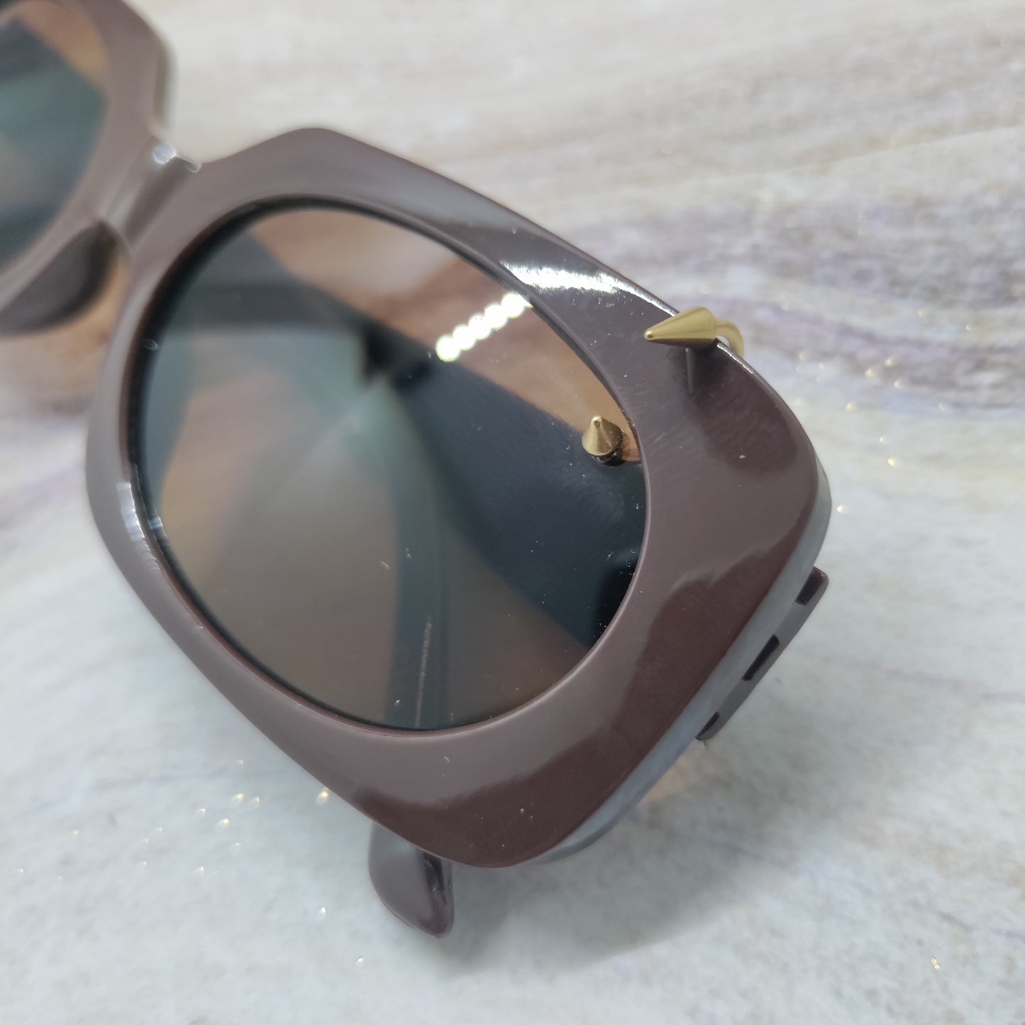 Close-up of a pair of sunglasses with a glossy dark brown frame and dark tinted lenses, resting on a light marble surface.