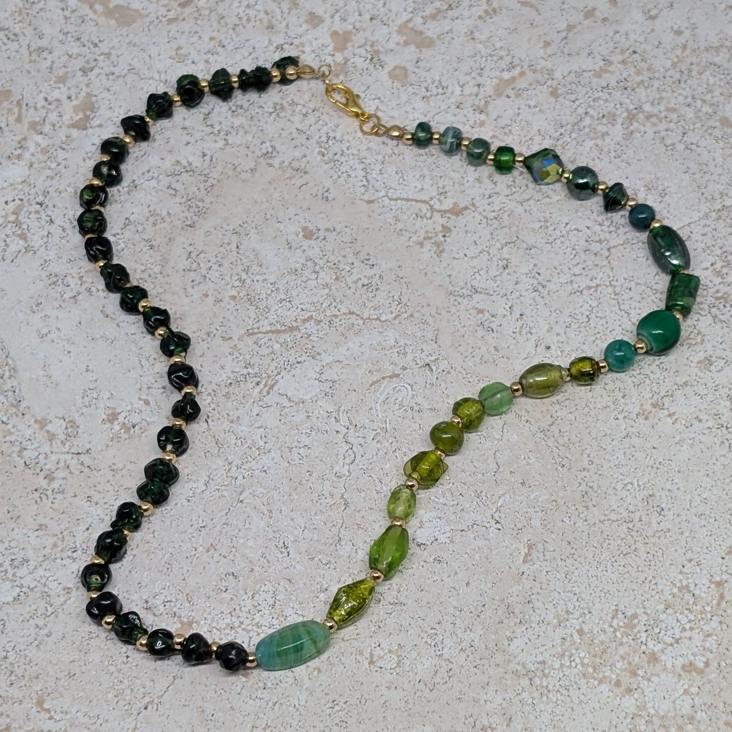 Necklace with green and black beads on a light stone surface