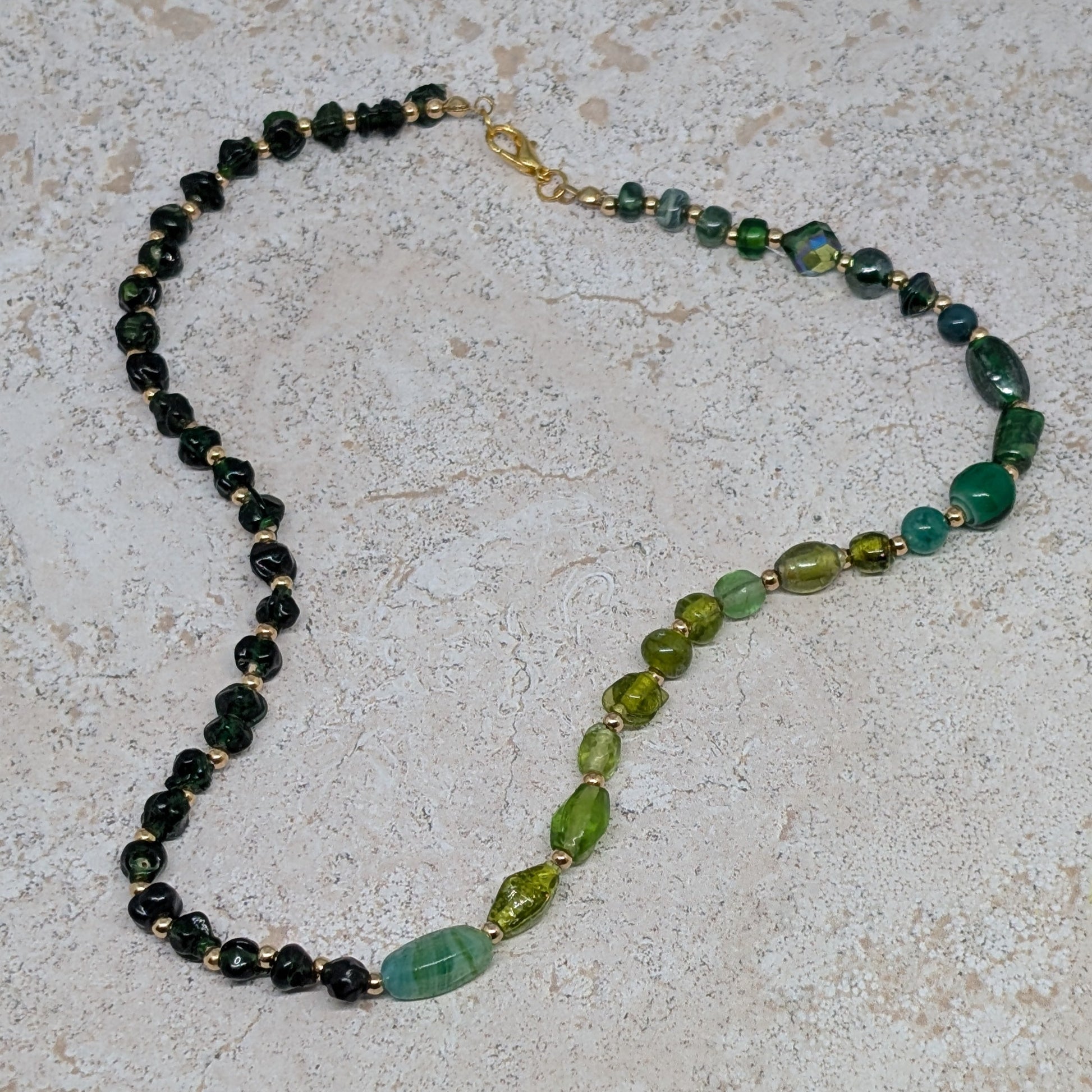 Necklace with green and black beads on a light stone surface