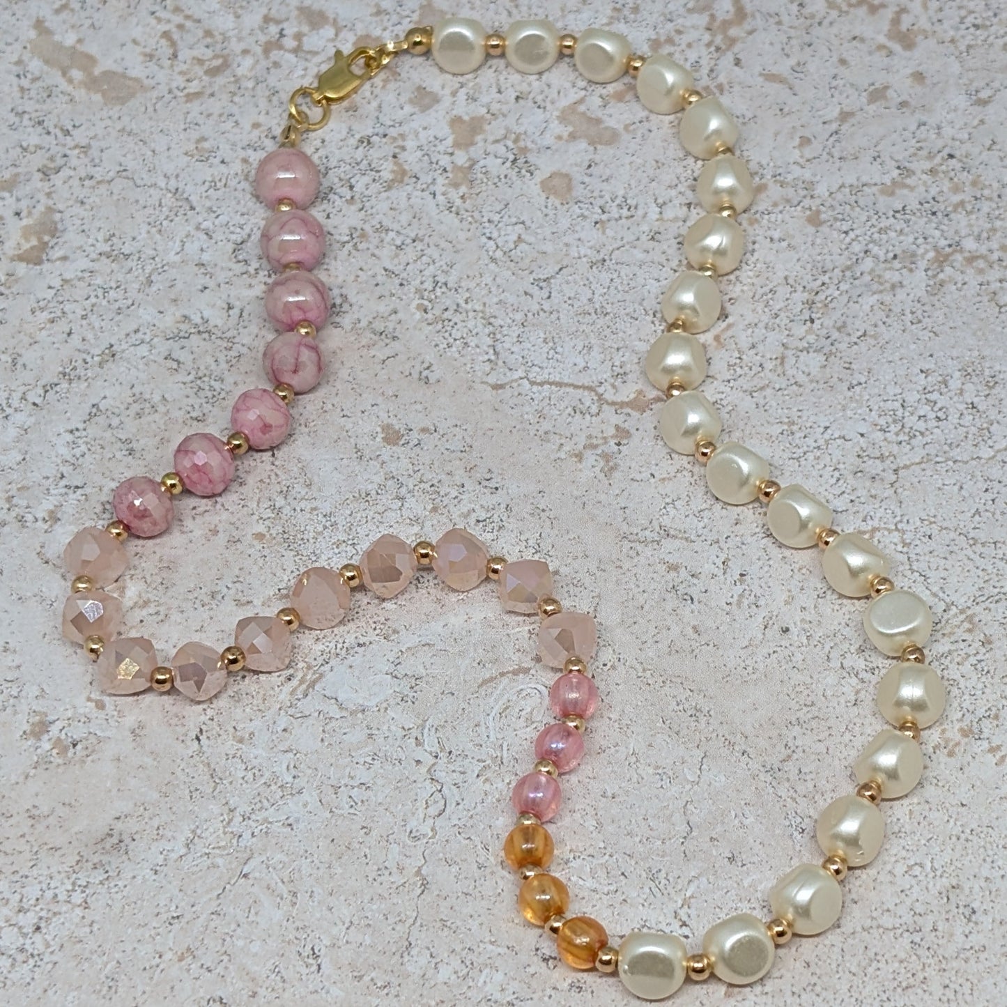 Necklace with pink, orange, and white beads on a light stone background