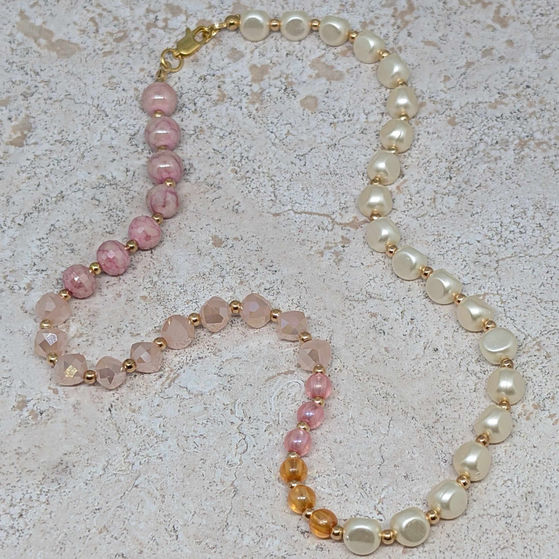 Necklace with pink, orange, and white beads on a light stone background