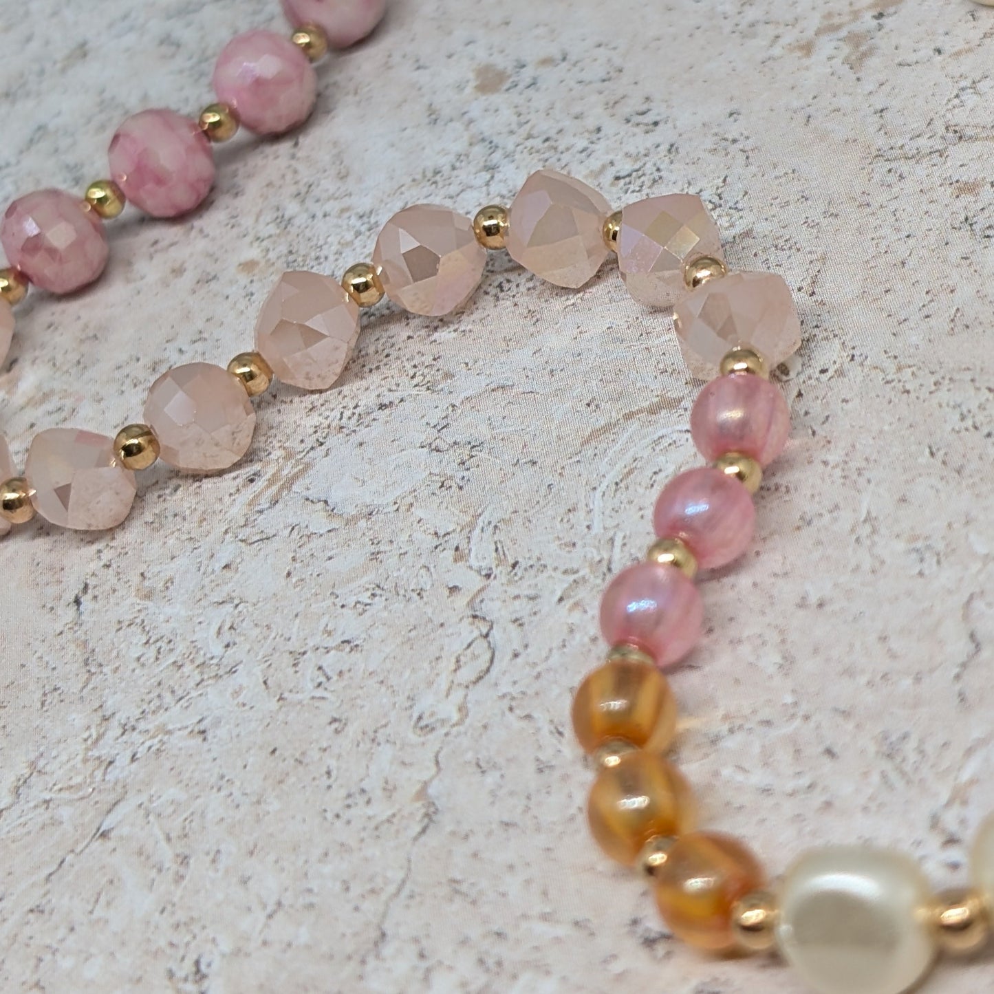 Necklace with pink, rose quartz, and gold beads on a light stone background