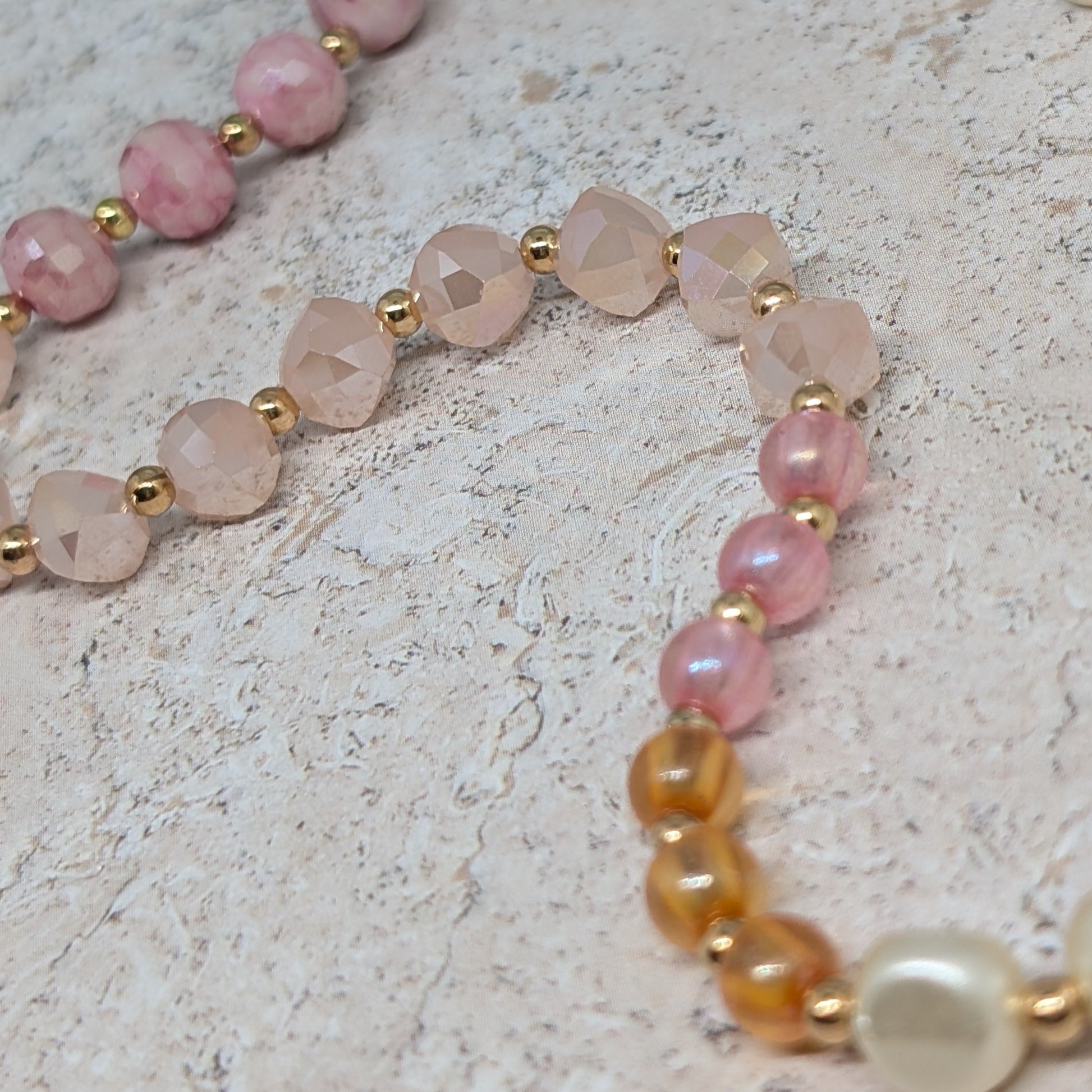 Necklace with pink, rose quartz, and gold beads on a light stone background
