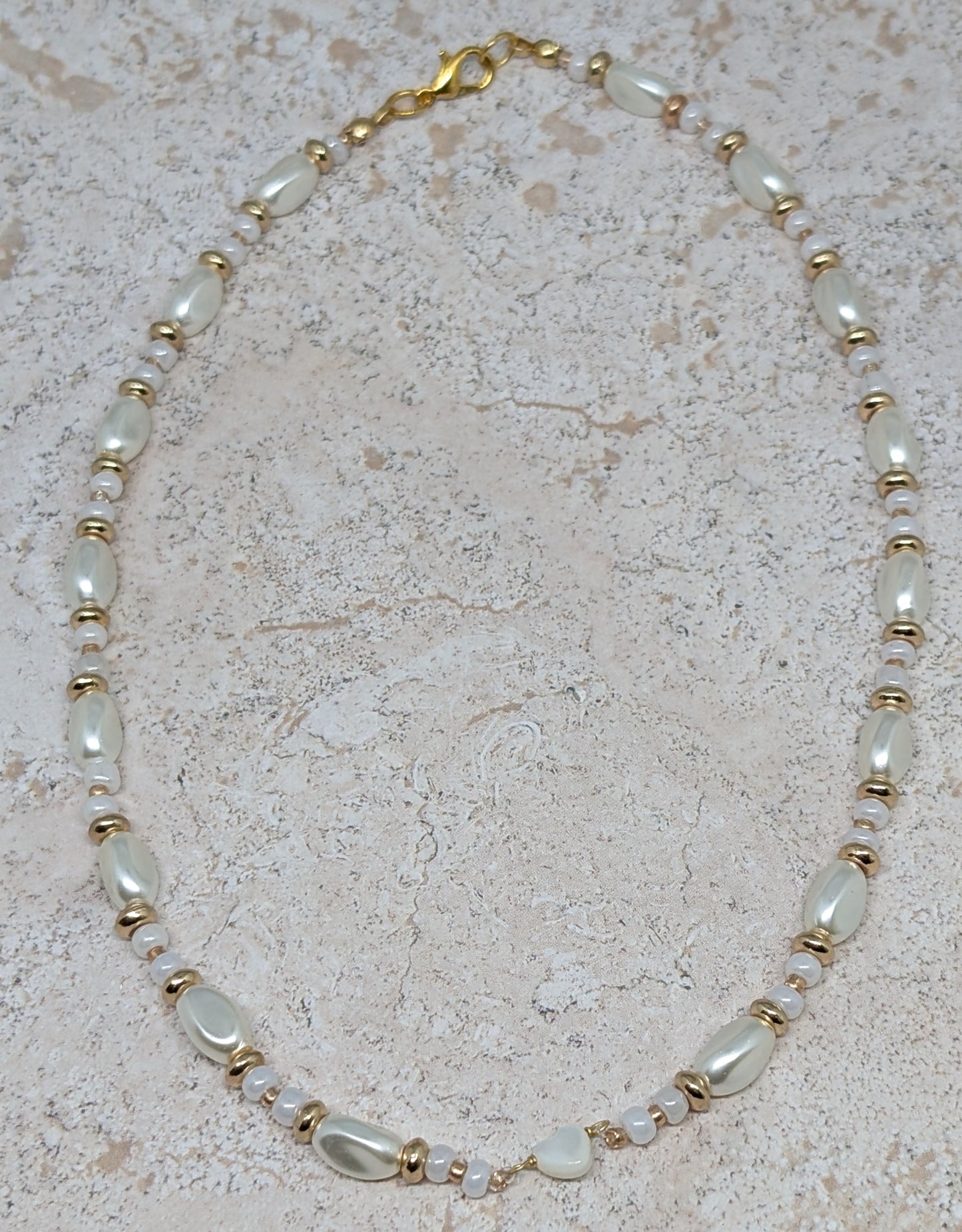 Necklace with pearls and gold accents on a beige stone surface