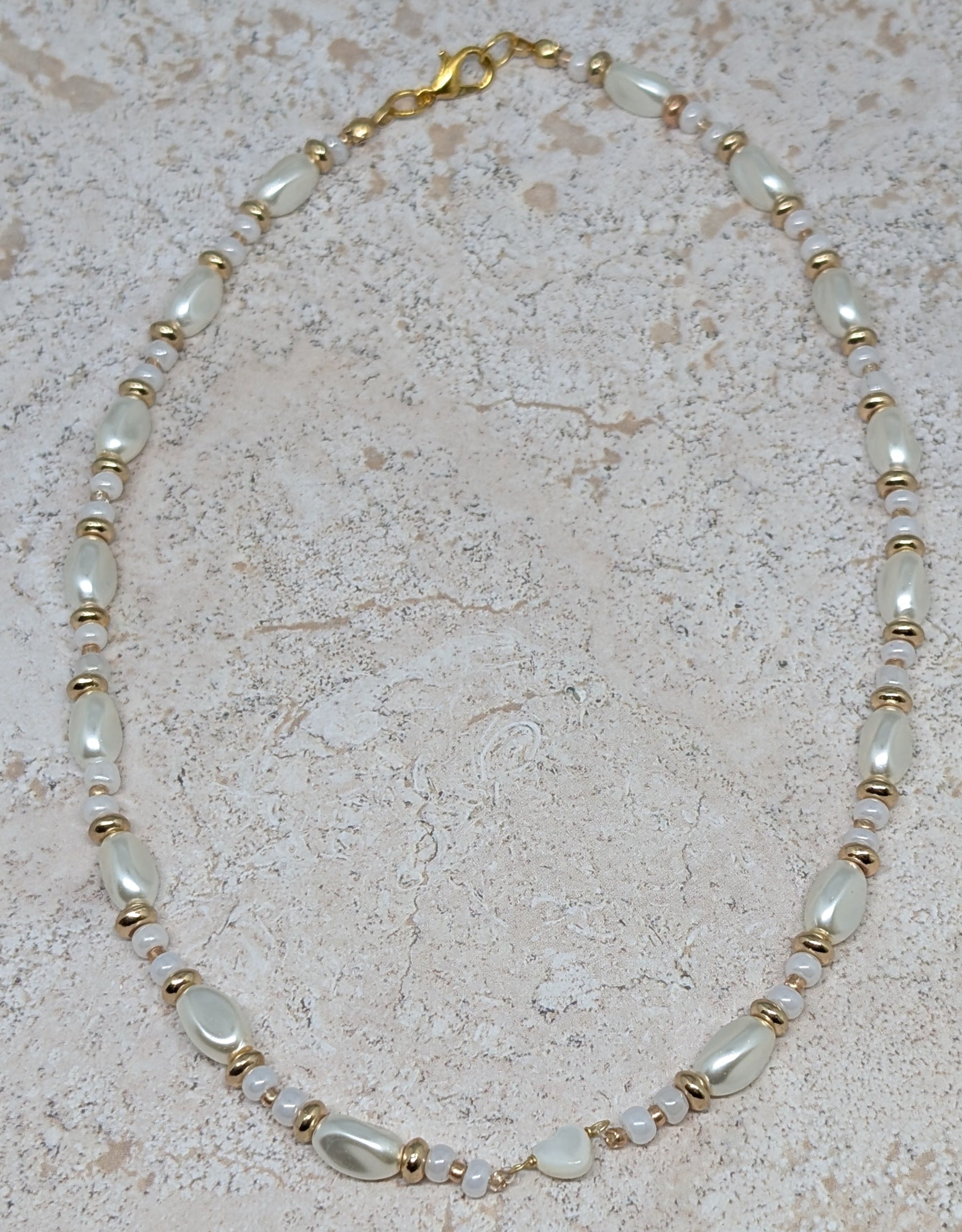 Necklace with pearls and gold accents on a beige stone surface