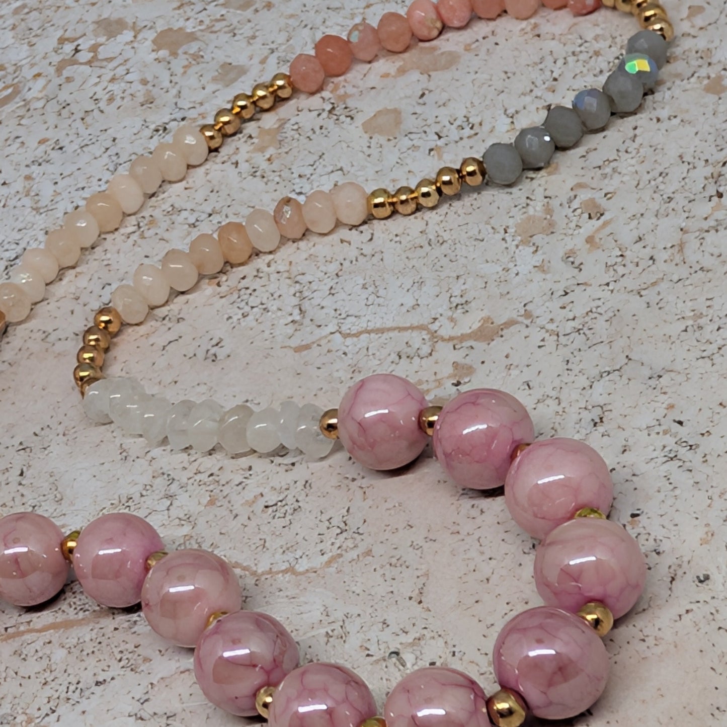 Necklace with pink beads and gold accents on a textured surface