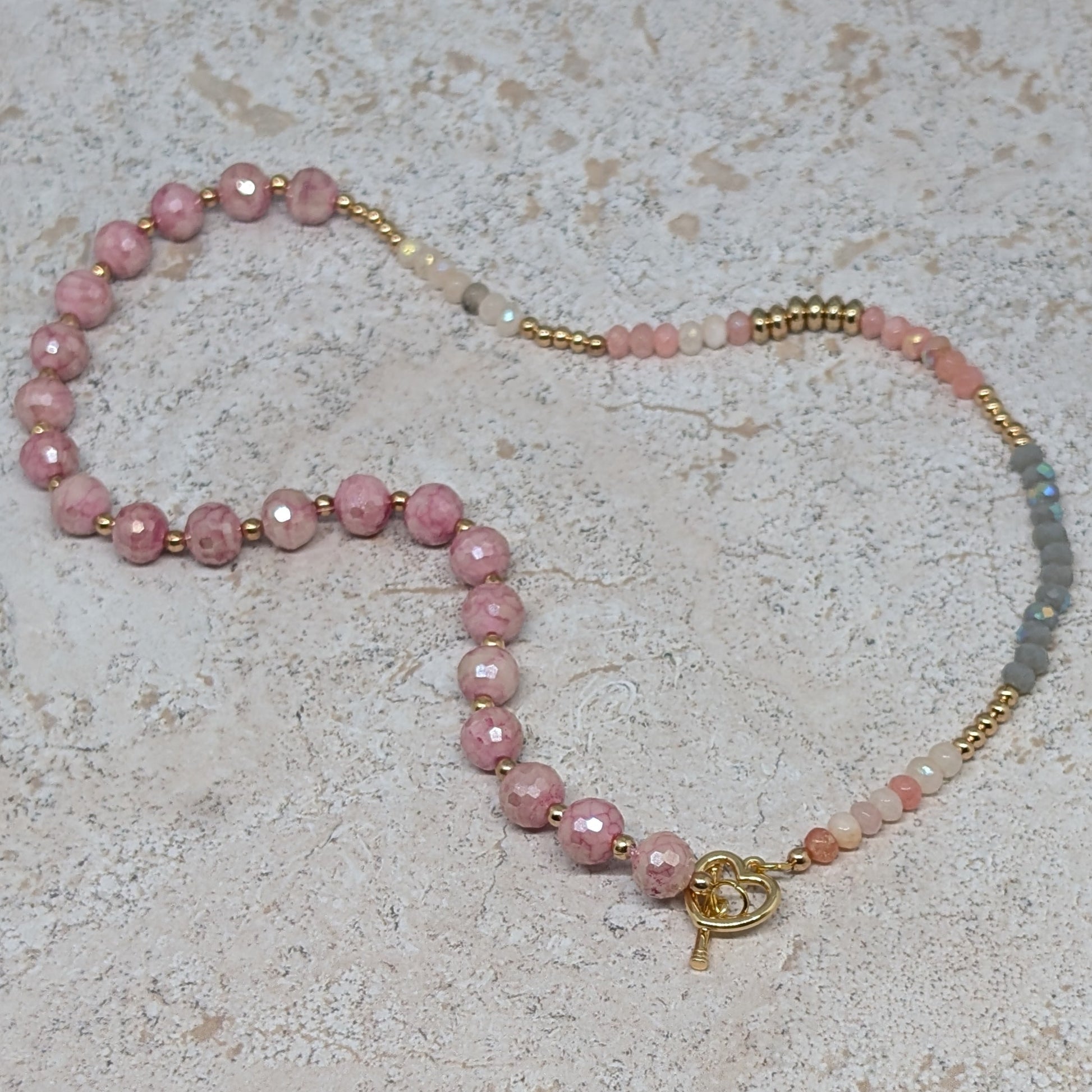 Beaded necklace with pink and gold elements on a textured surface