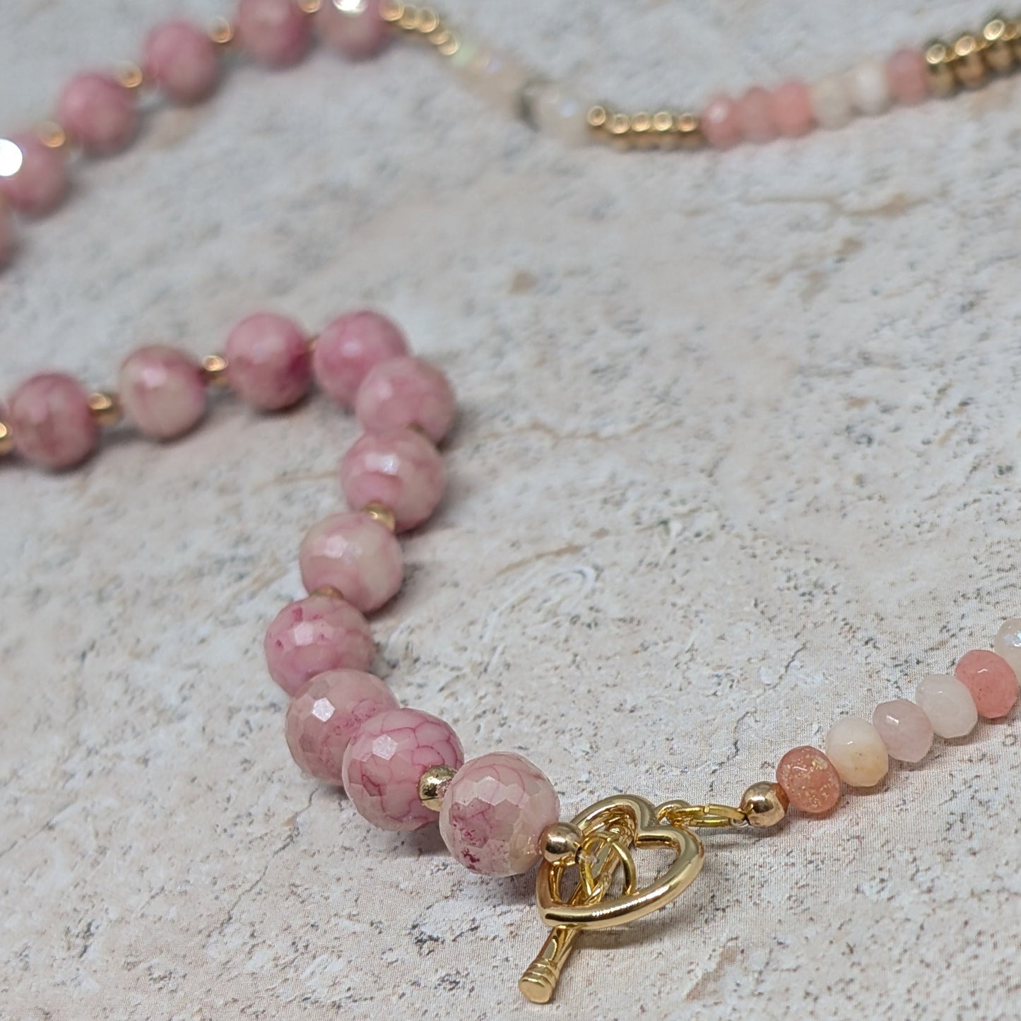 Necklace with pink beads and a gold clasp on a light stone surface