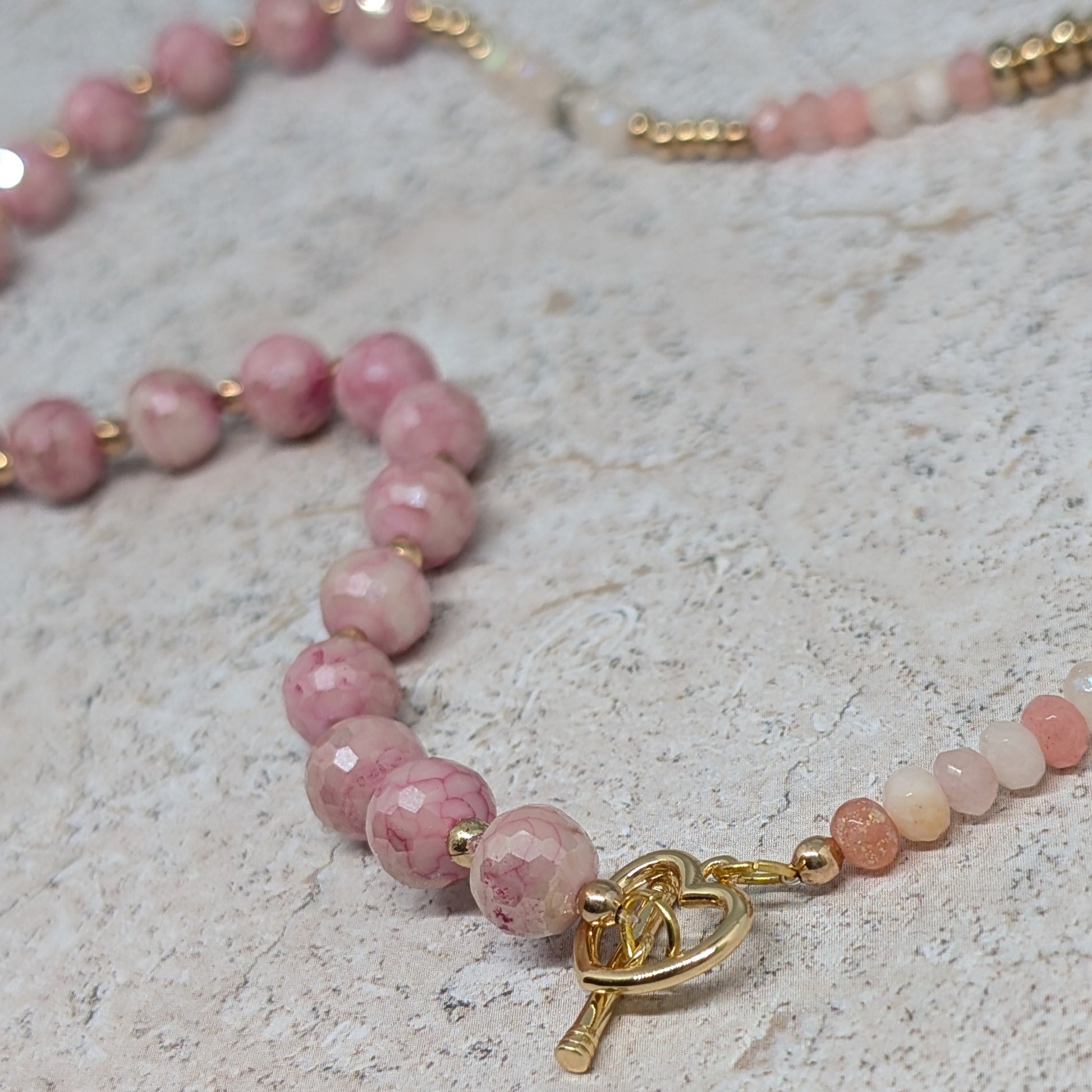 Necklace with pink beads and a gold clasp on a light stone surface