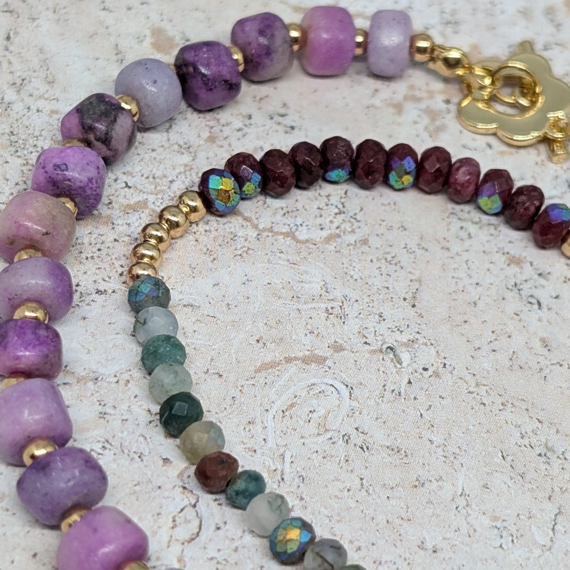 Two beaded bracelets with purple, green, and gold beads on a textured surface.