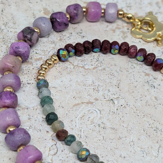 Two beaded bracelets with purple, green, and gold beads on a textured surface.