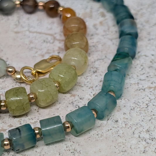 Beaded bracelets with green and gold accents on a textured surface