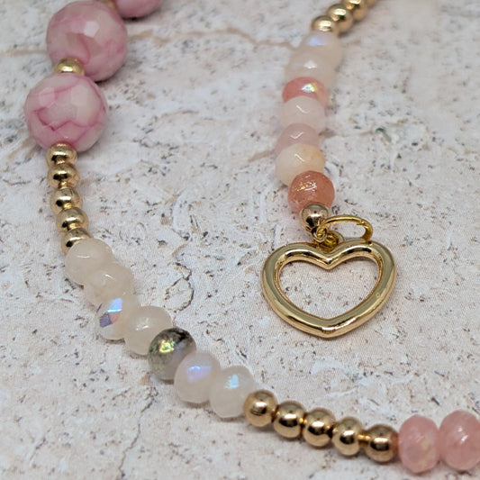 Necklace with pink beads and a gold heart charm on a light surface