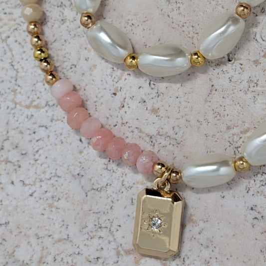 Necklace with pearls, pink beads, and a gold tag on a textured surface