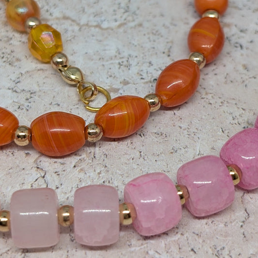 Two beaded bracelets with orange, pink, and gold beads on a textured surface.