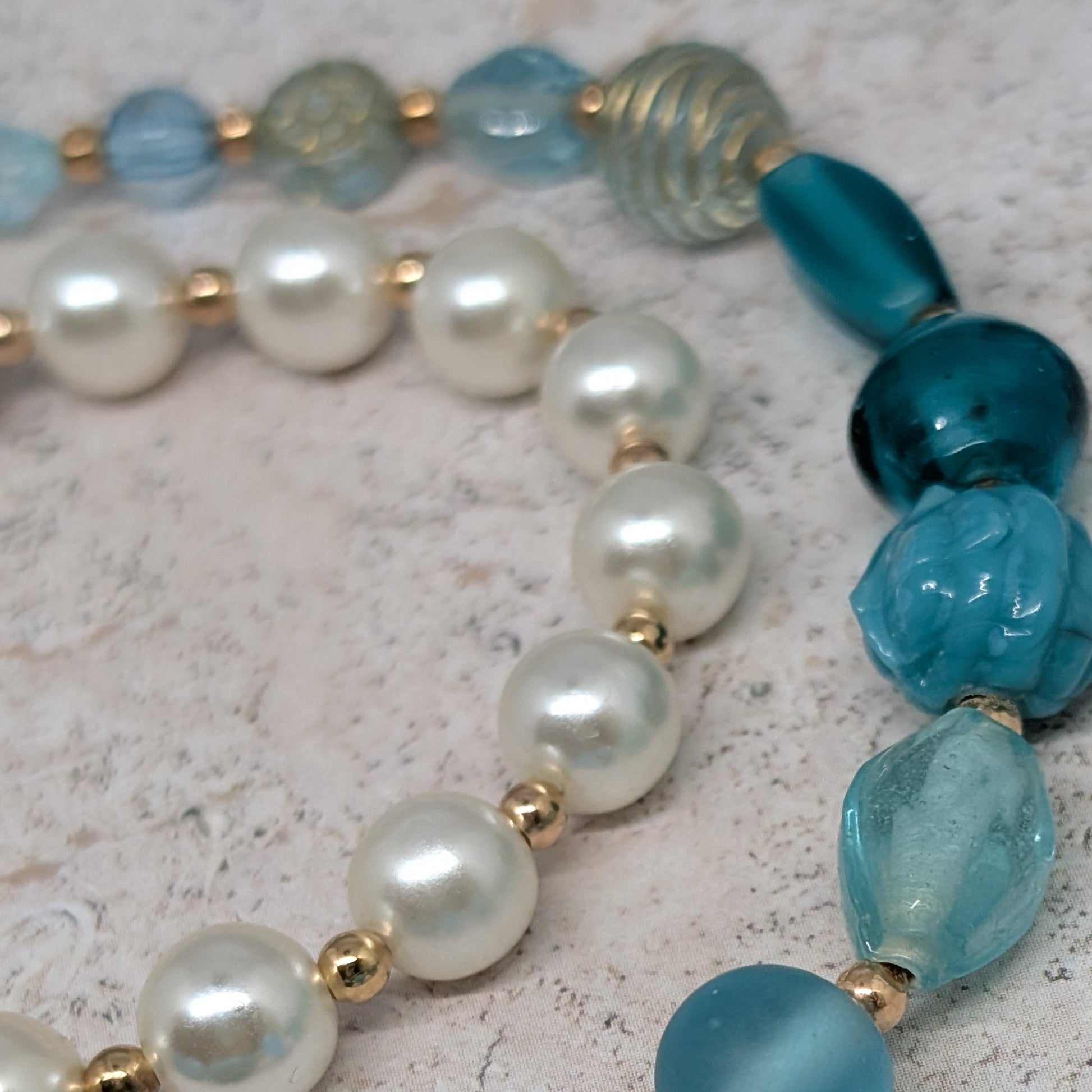 Beaded necklace with blue and white pearls on a textured surface
