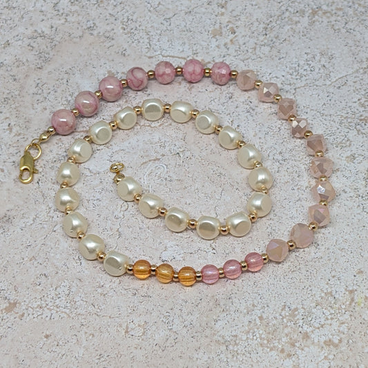 Beaded necklace with pink, white, and gold beads on a textured surface