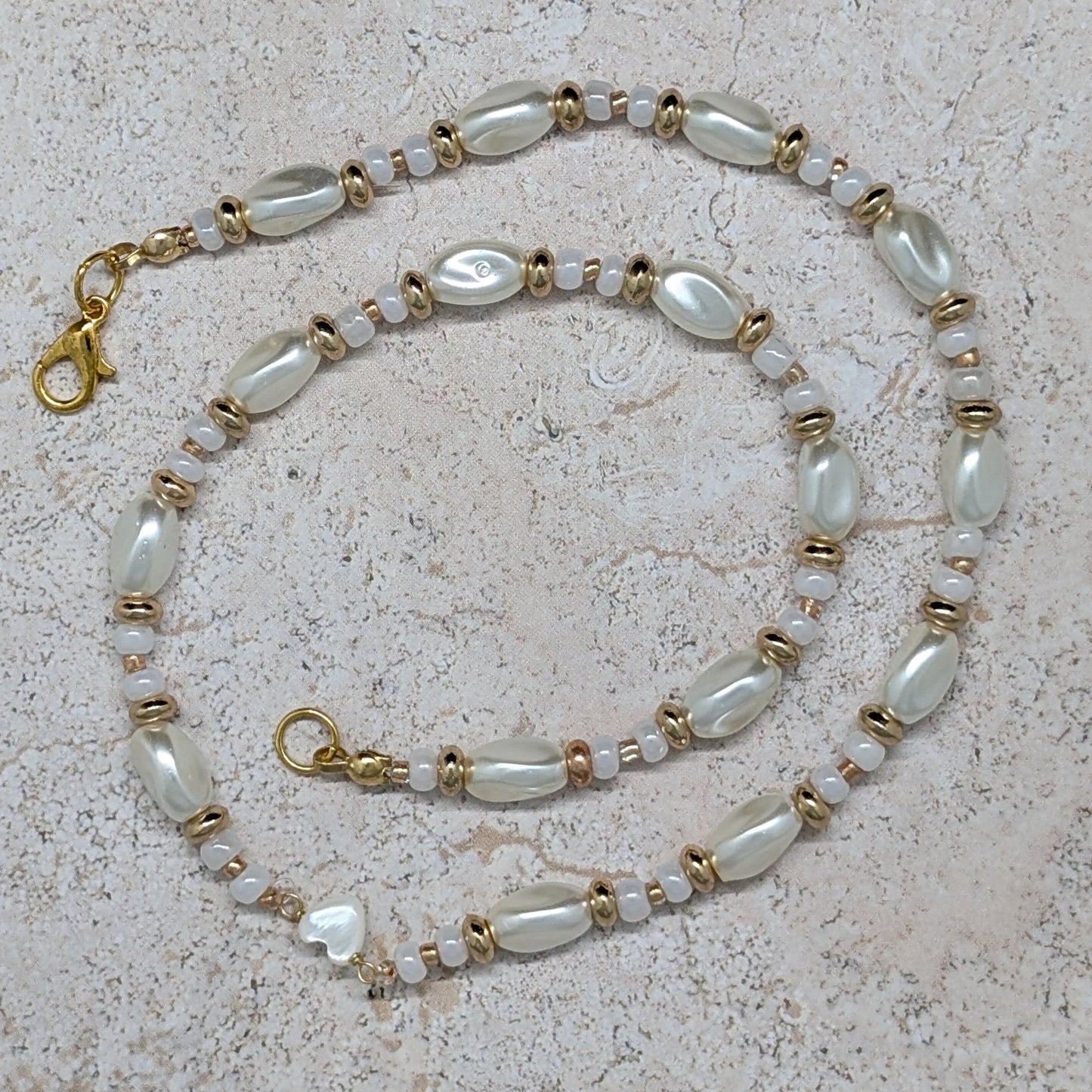 Pearl and gold chain necklace on a beige stone surface