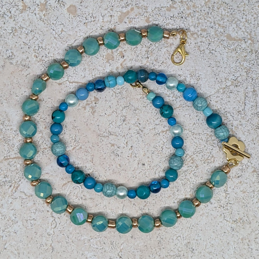 Two turquoise beaded necklaces with gold clasps on a light gray surface