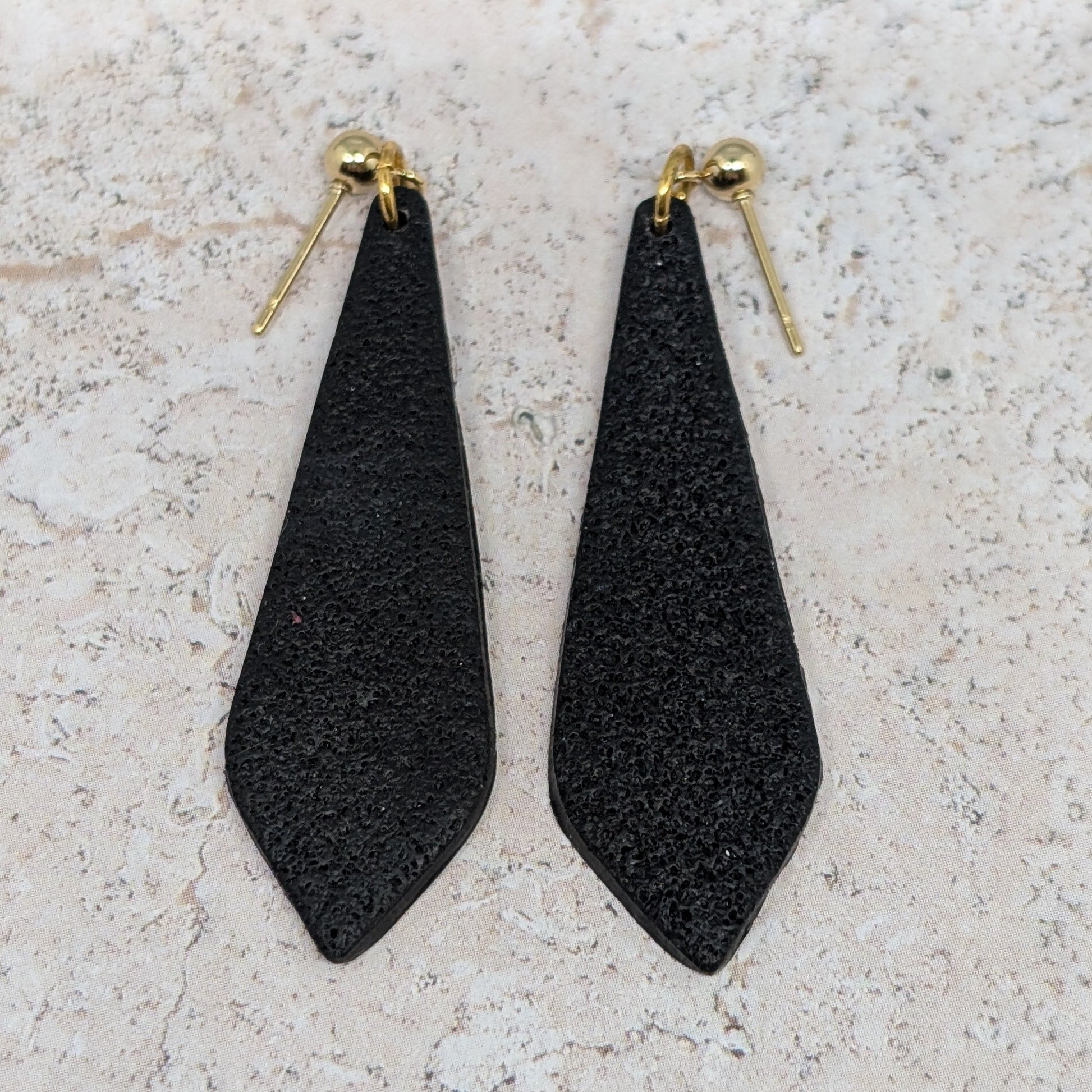Black teardrop-shaped earrings on a light stone surface