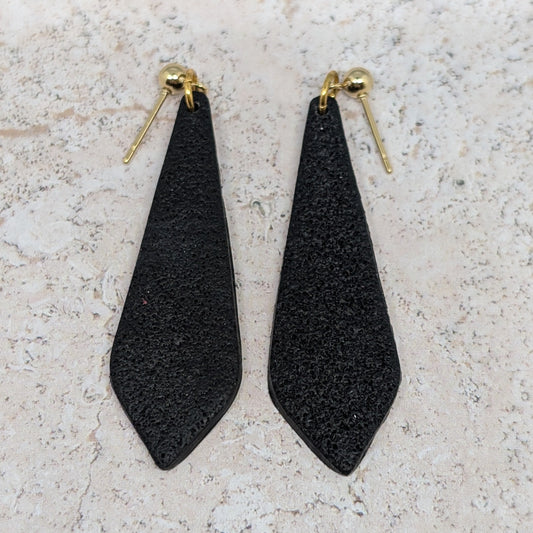 Black teardrop-shaped earrings on a light stone surface