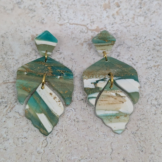 Pair of green and white ceramic earrings on a textured surface