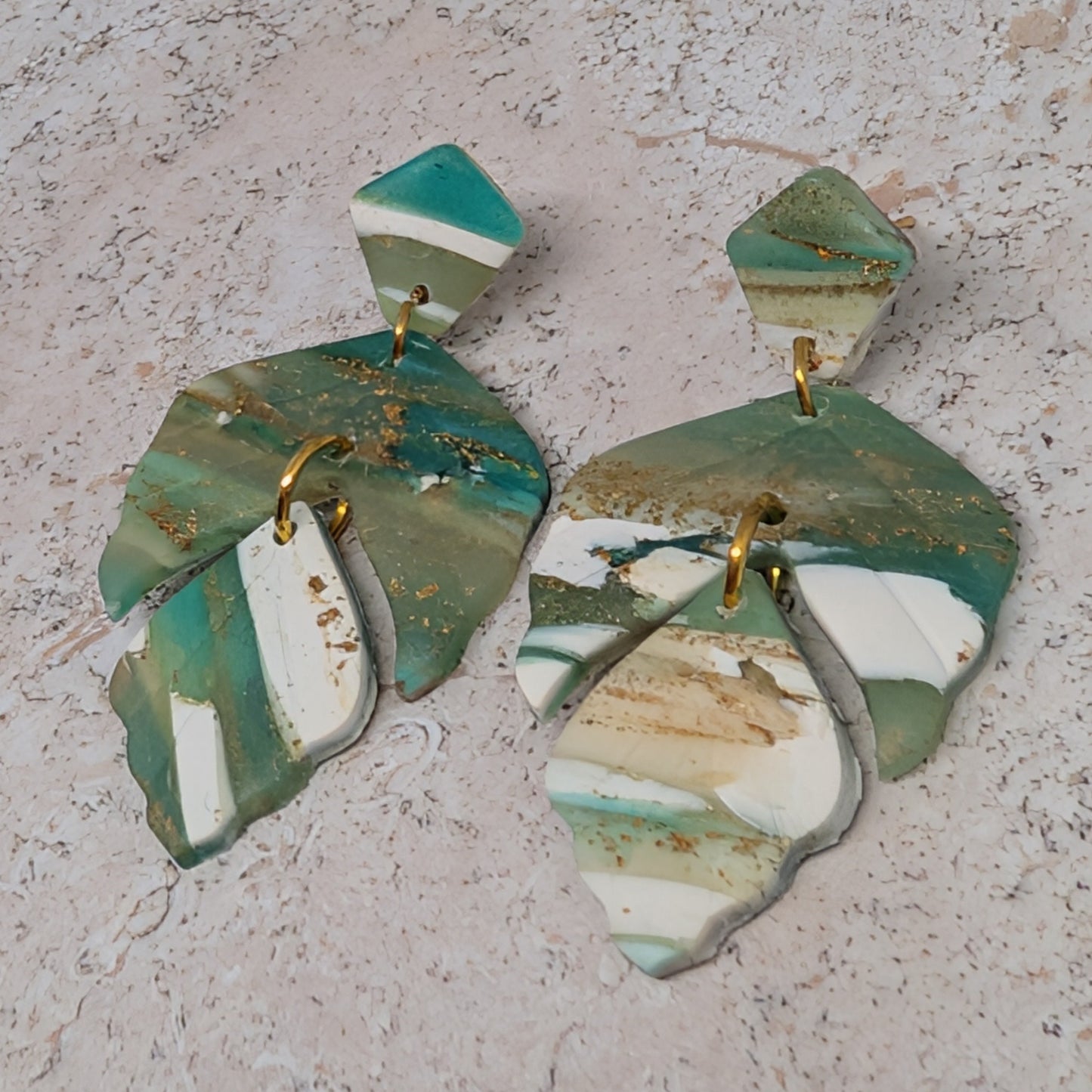 Pair of green and white earrings on a textured surface