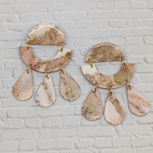 Pair of pink and gold earrings on a white brick wall background
