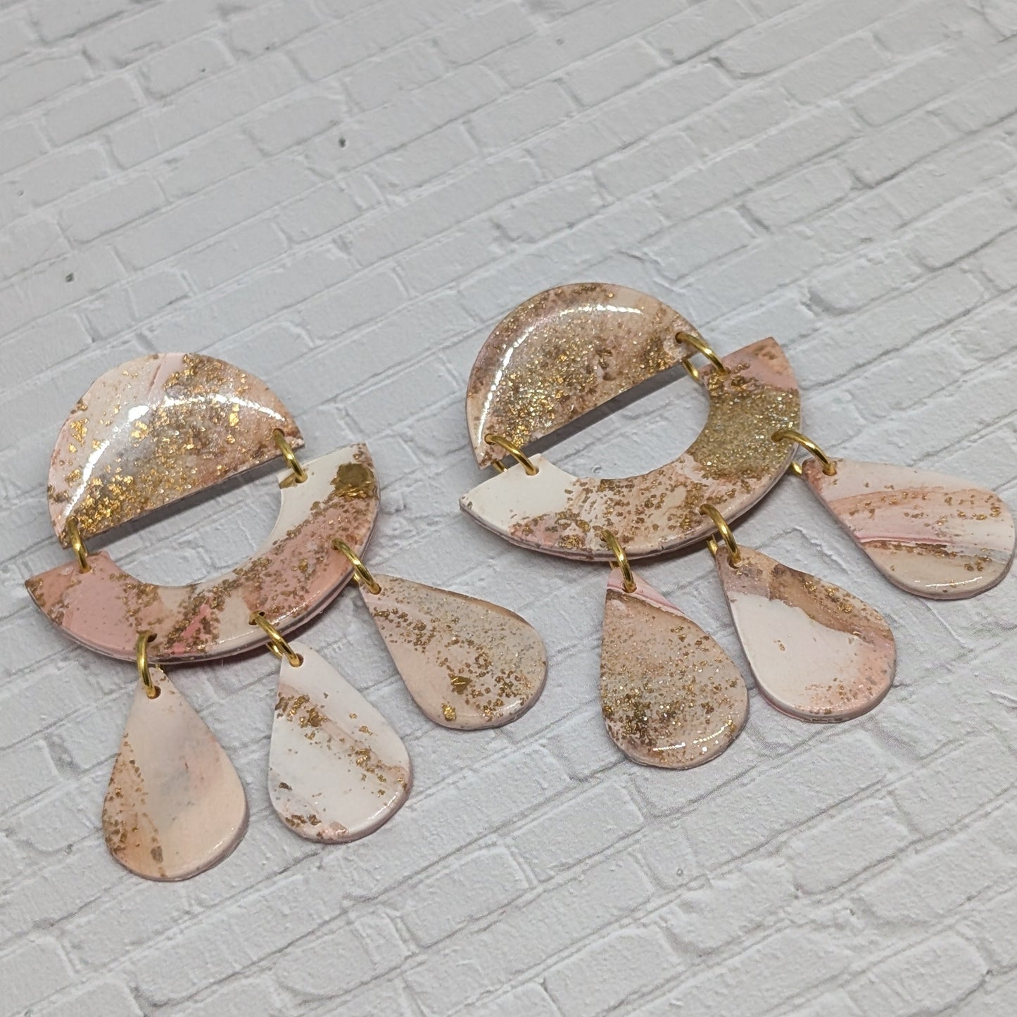 Pair of earrings with pink and gold accents on a light gray brick background