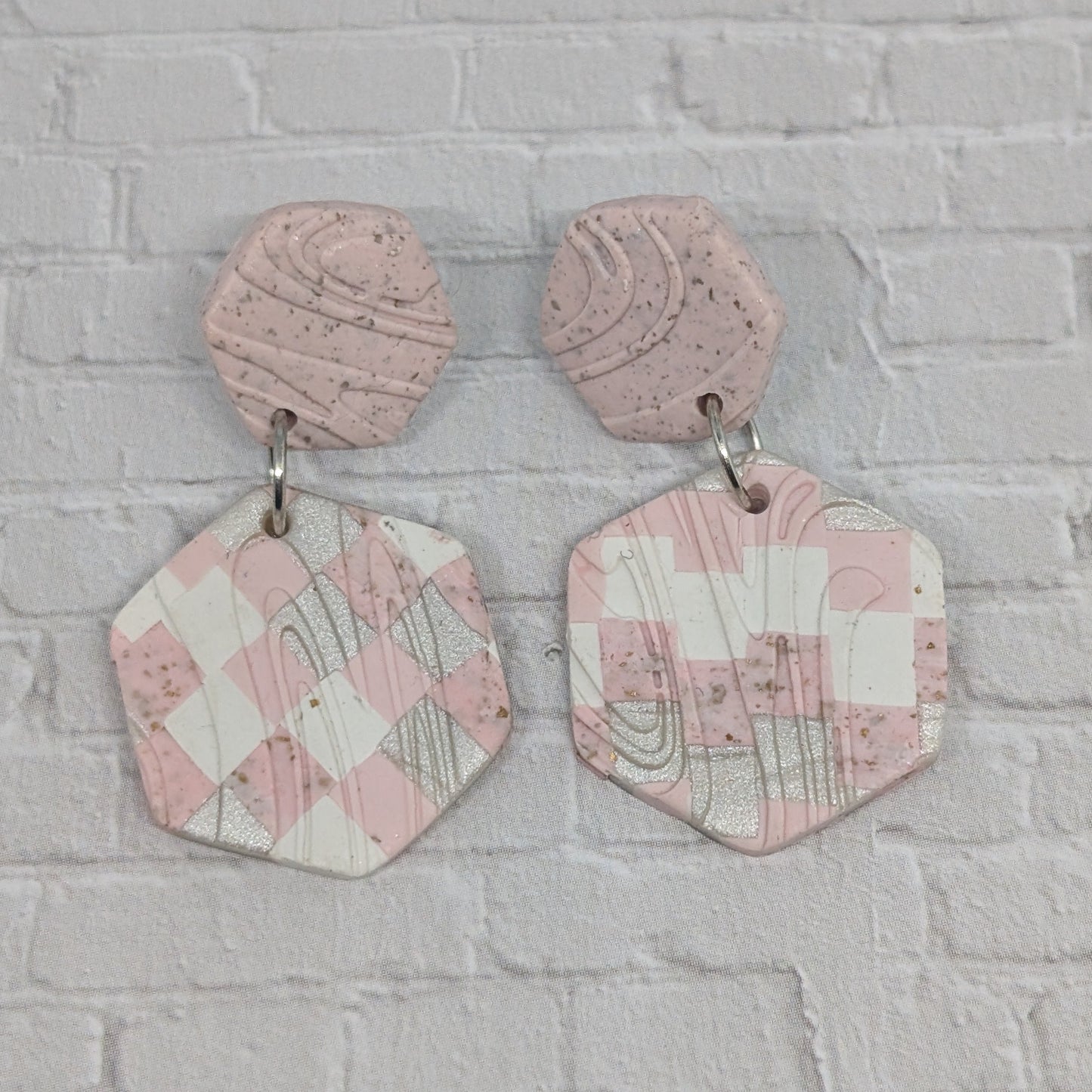 Pink geometric earrings on a gray brick wall background