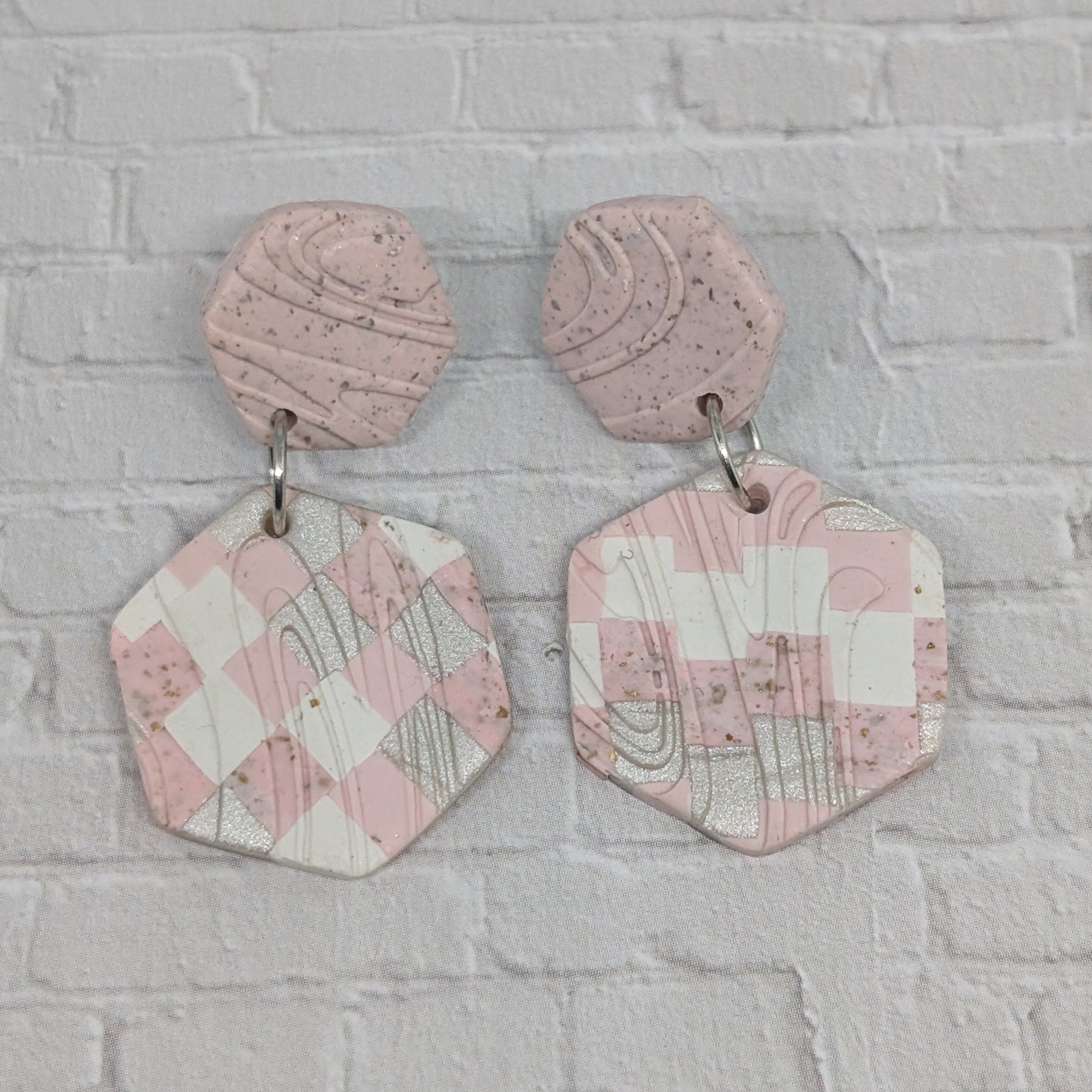 Pink geometric earrings on a gray brick wall background