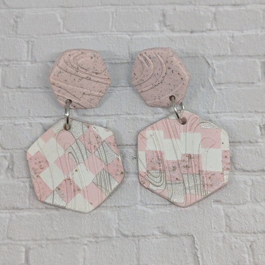 Pink geometric earrings on a gray brick wall background