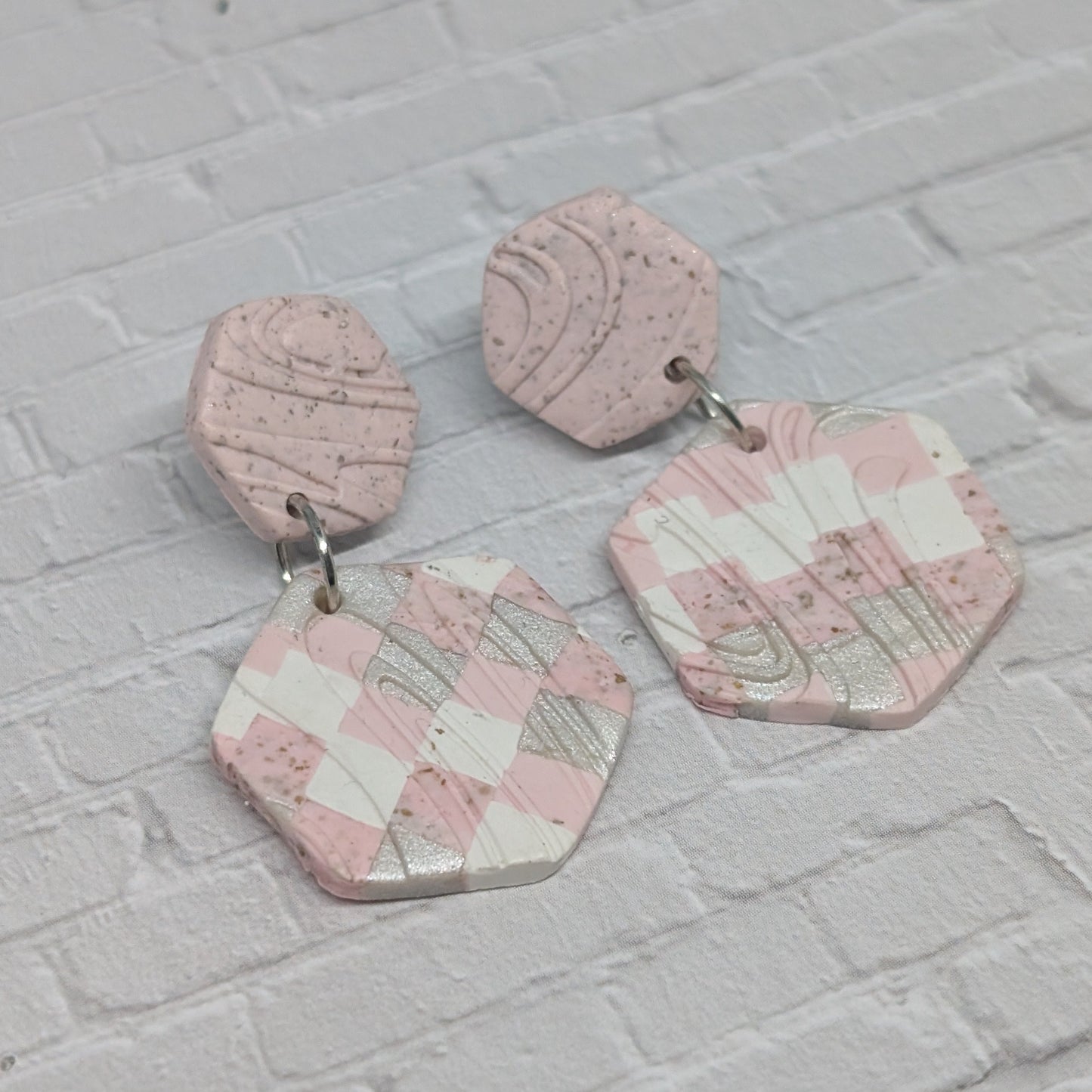 Hexagonal pink and white checkered earrings on a light gray brick background