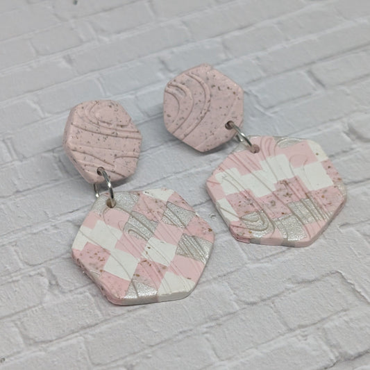 Hexagonal pink and white checkered earrings on a light gray brick background