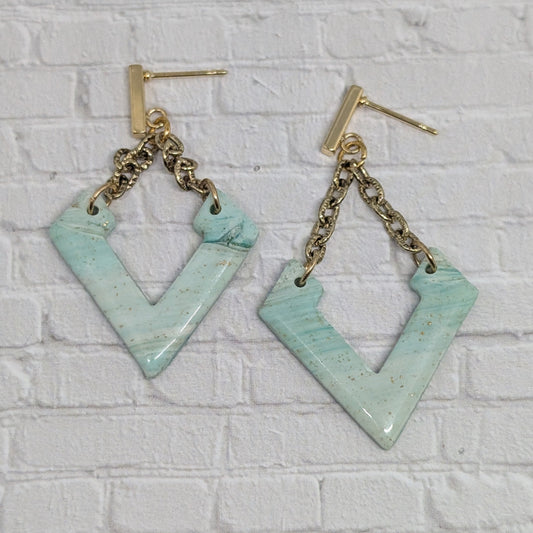 Pair of turquoise earrings with gold chains on a white brick wall background