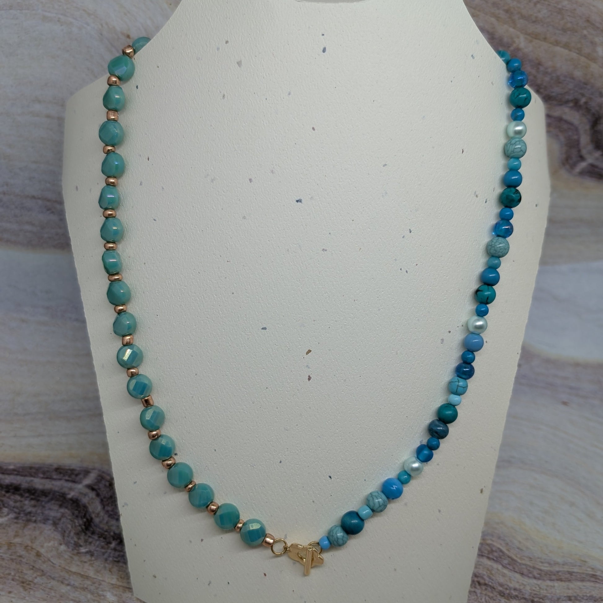 Turquoise beaded necklace on a white bust against a stone background