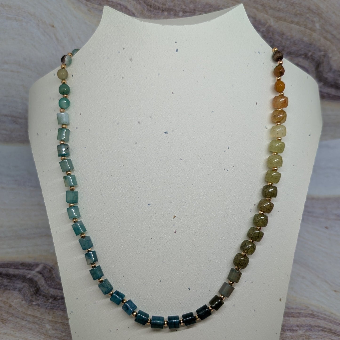Necklace with multicolored beads on a white mannequin bust against a marble background