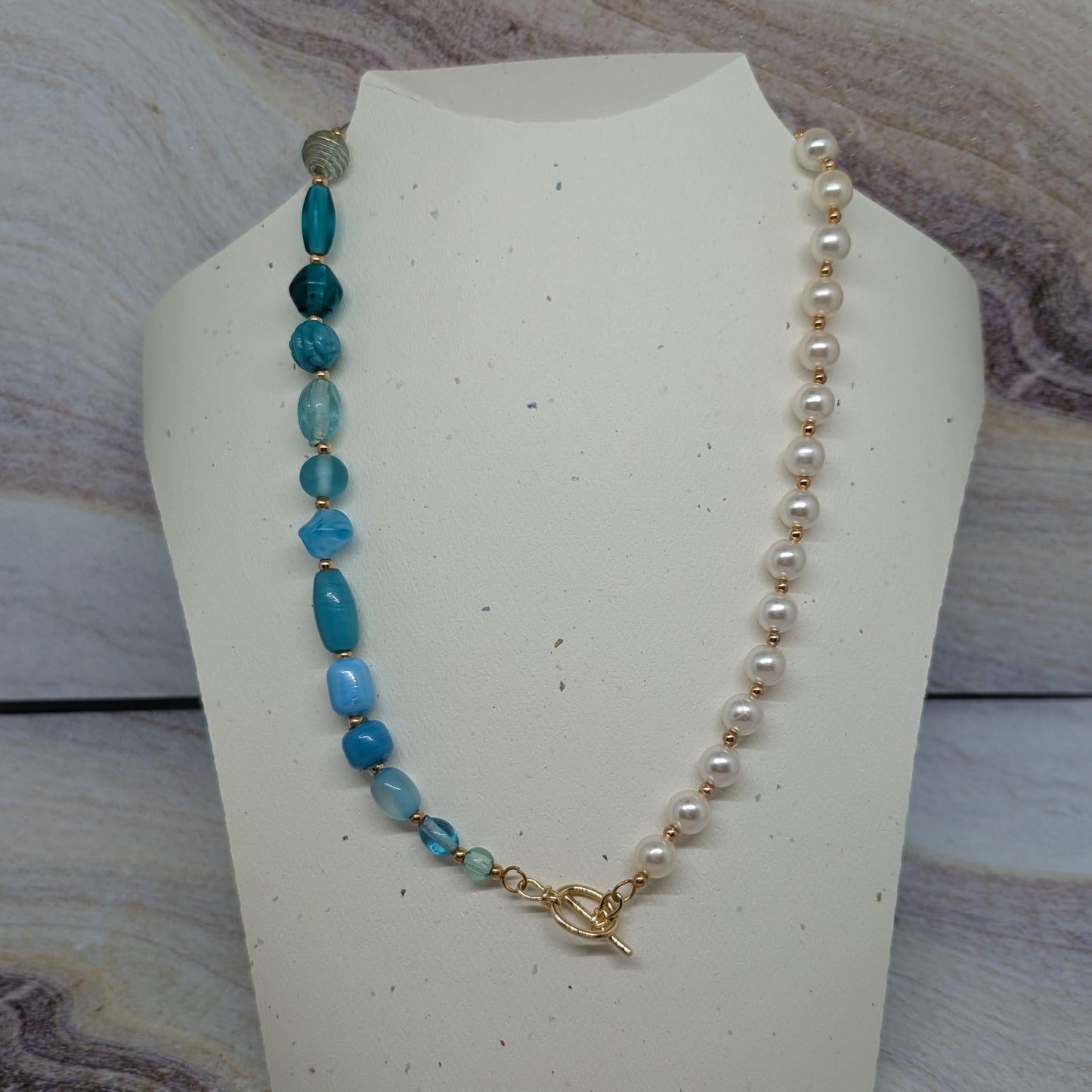 Necklace with blue and white beads on a mannequin bust against a marble background