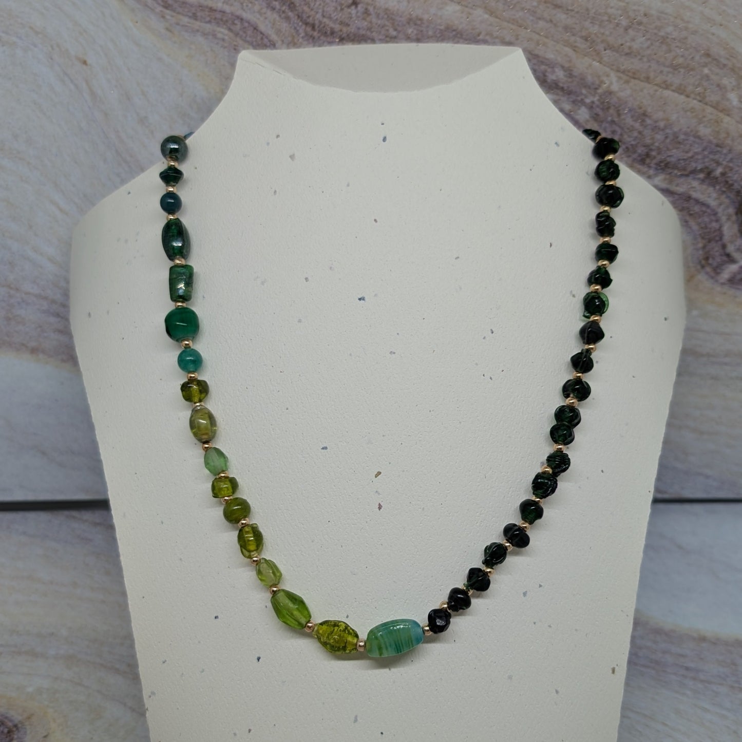 Necklace with green and black beads on a white mannequin bust against a marbled background