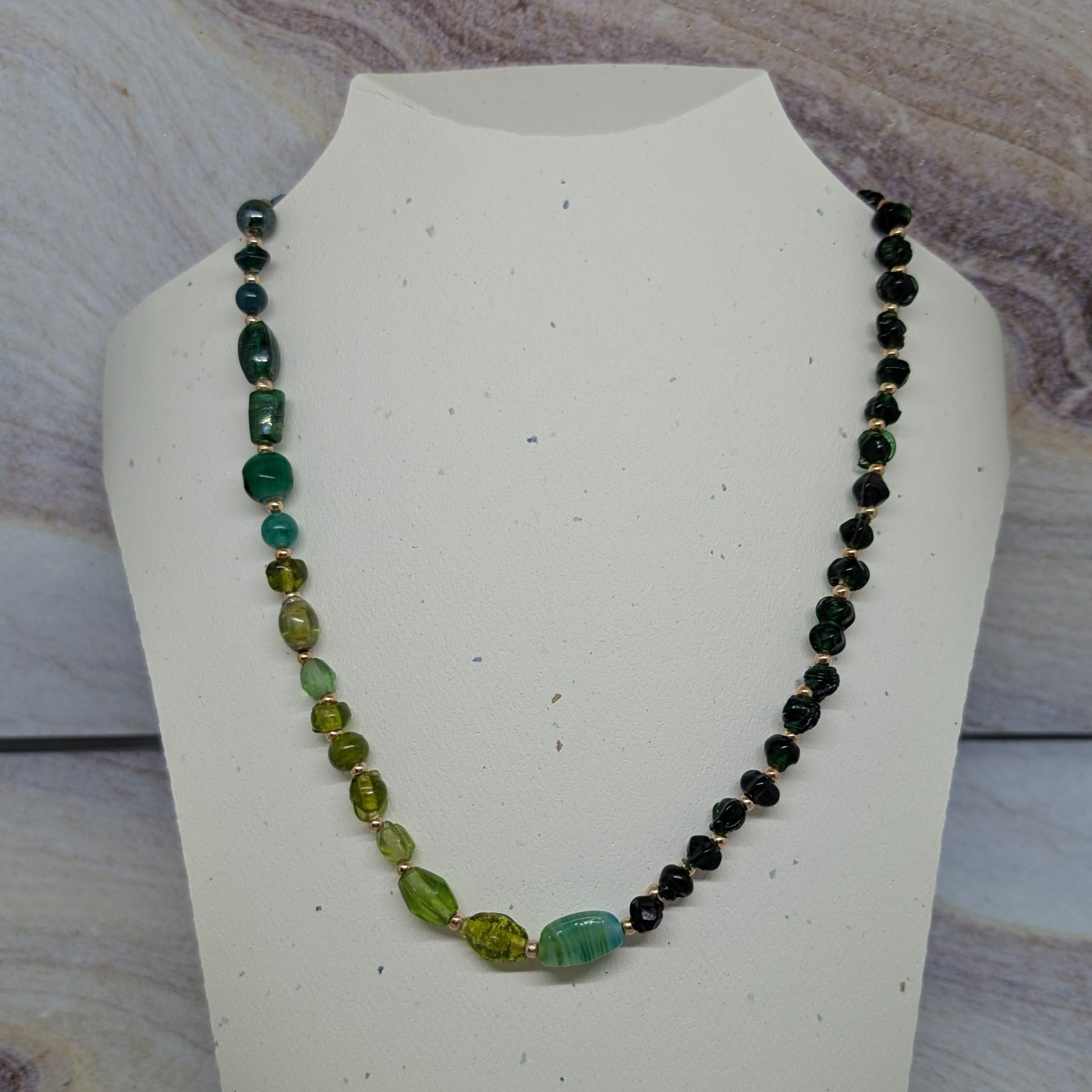 Necklace with green and black beads on a white mannequin bust against a marbled background