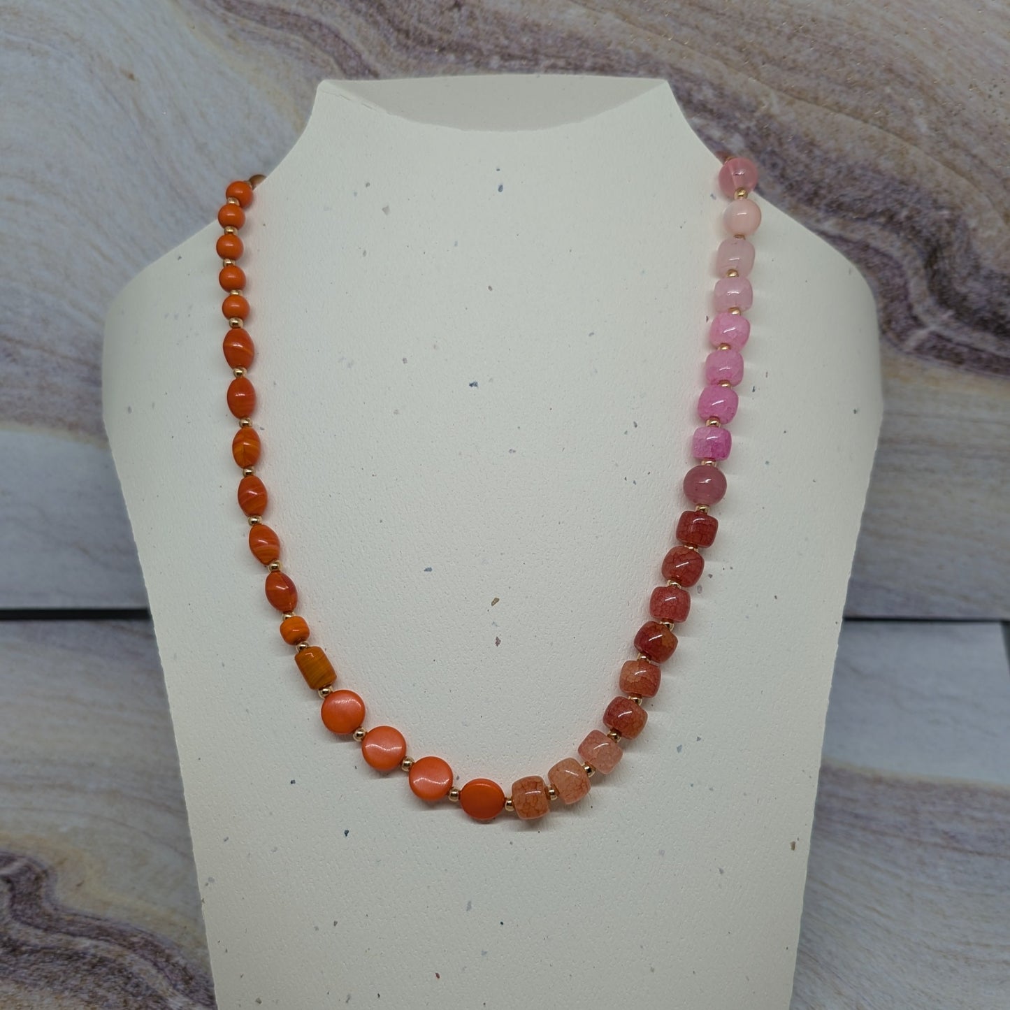 Necklace with orange and pink beads on a mannequin bust against a marble background