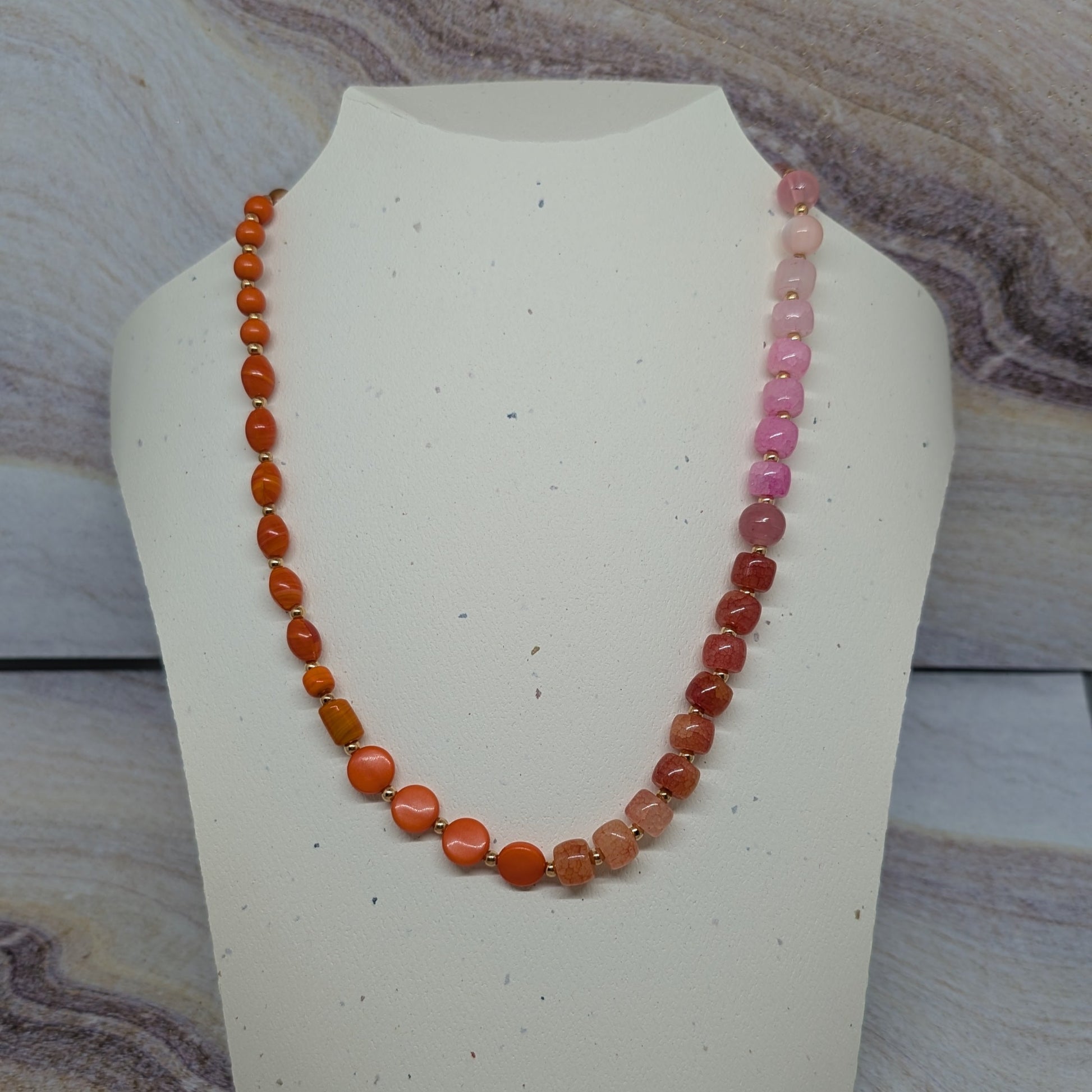 Necklace with orange and pink beads on a mannequin bust against a marble background