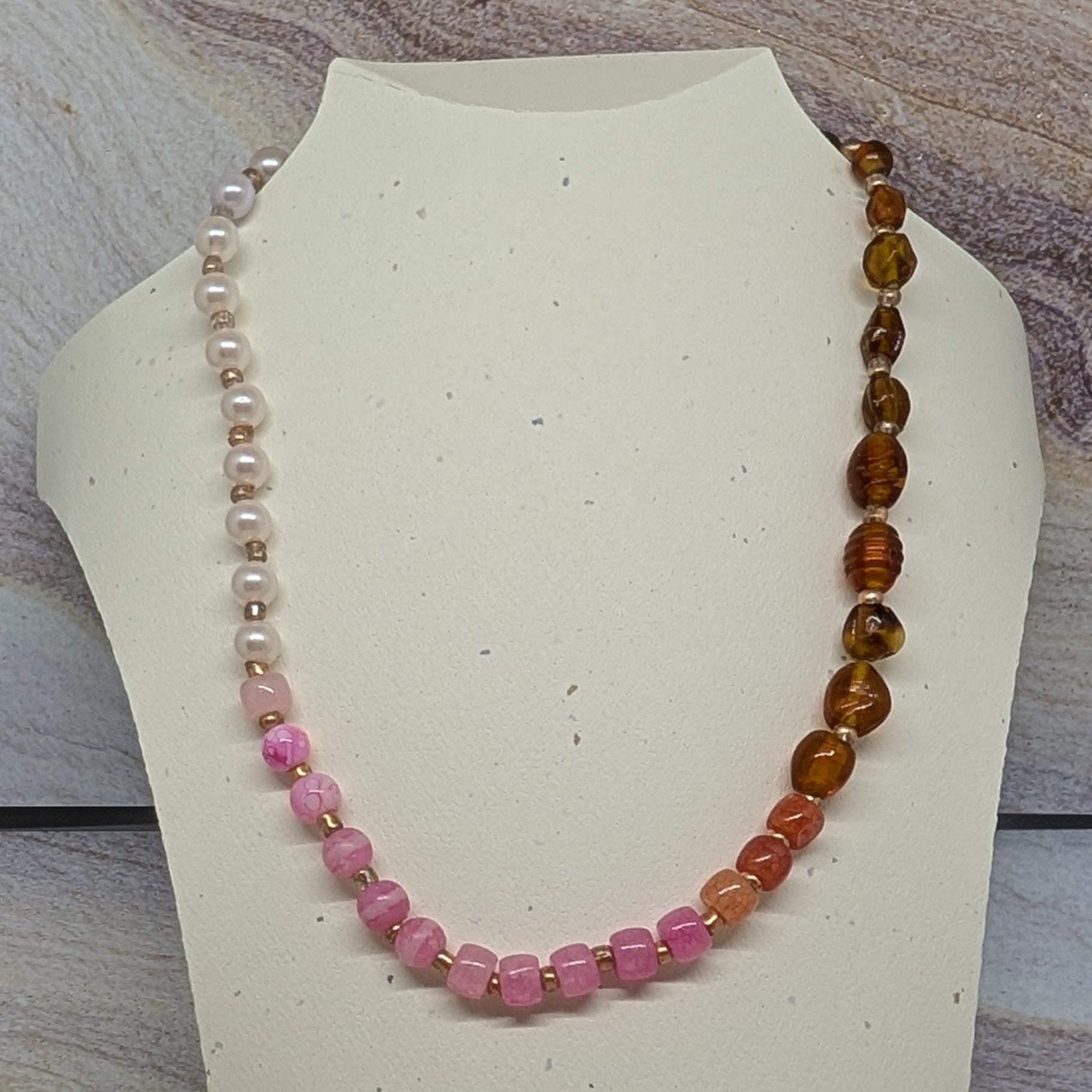 Necklace with multicolored beads on a mannequin bust against a marble background