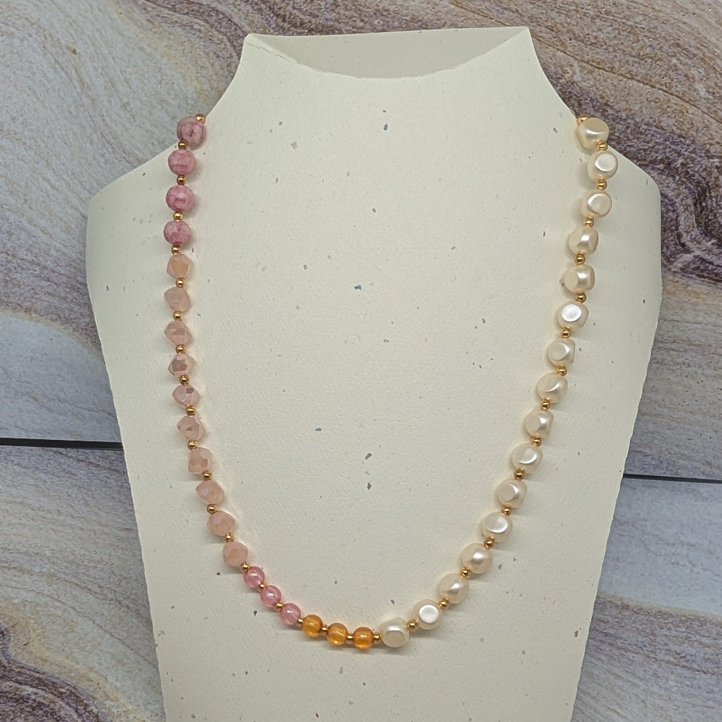 Necklace with multicolored beads on a mannequin bust against a marble background
