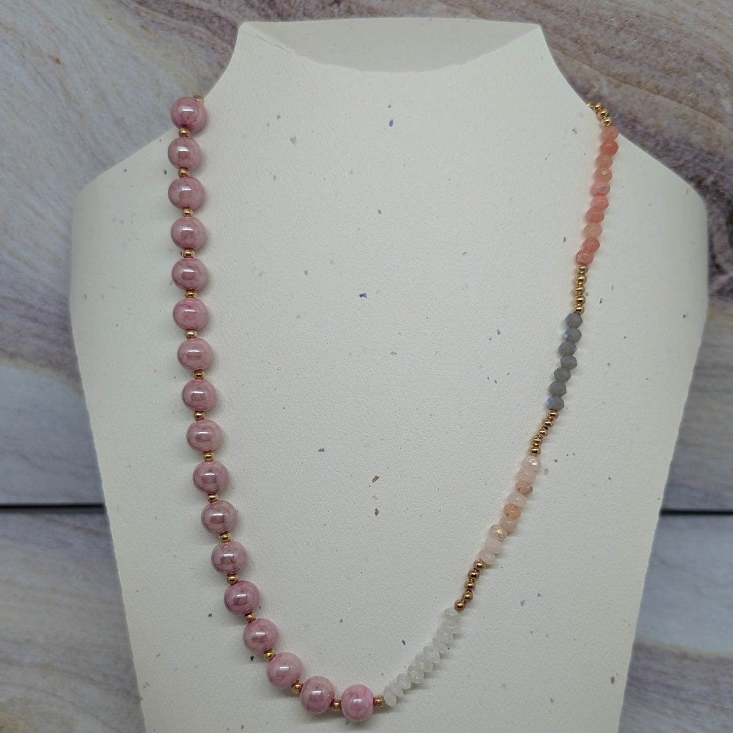 Necklace with pink and white beads on a white bust against a marble background