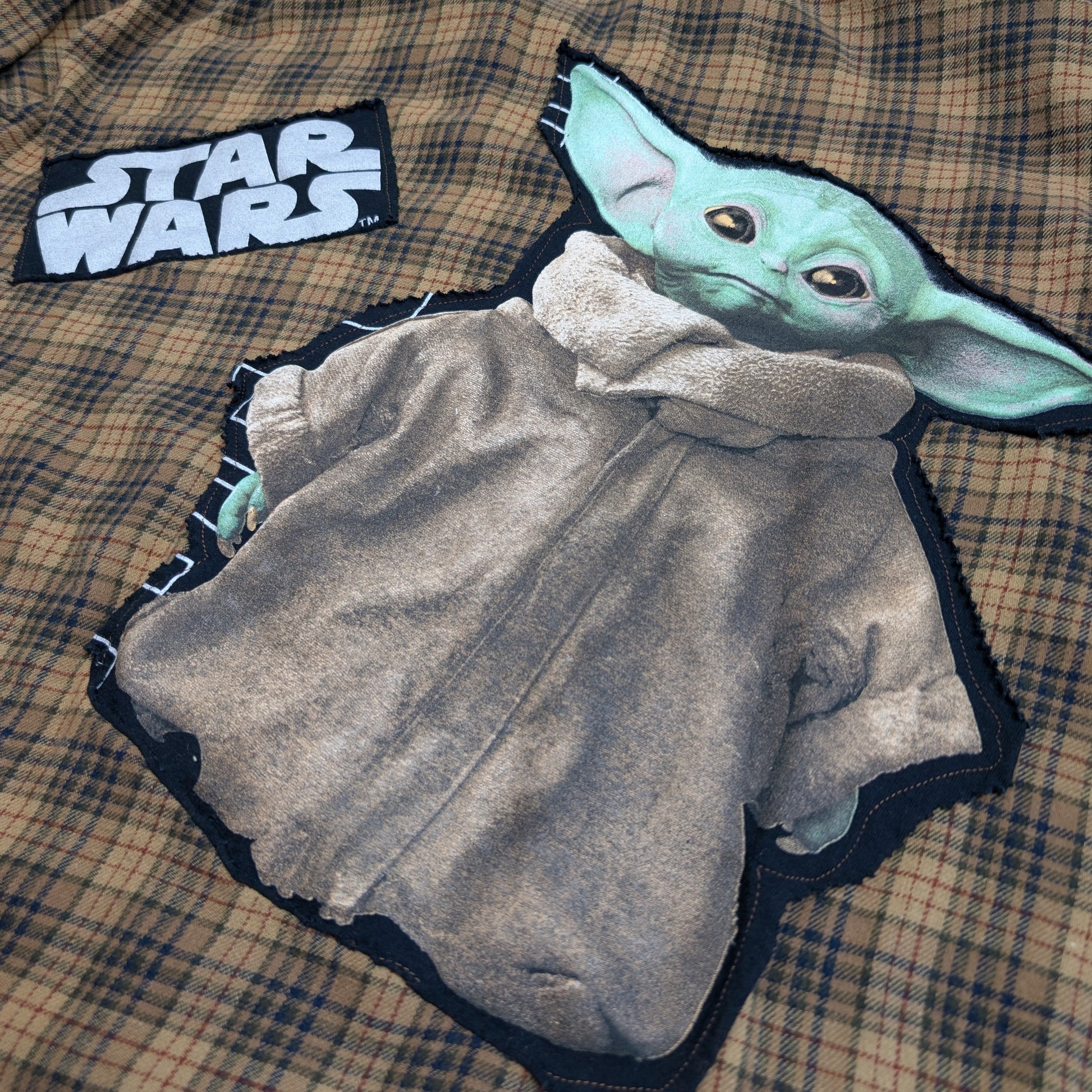 Plaid shirt with 'Star Wars' logo and Baby Yoda design on a checkered fabric background