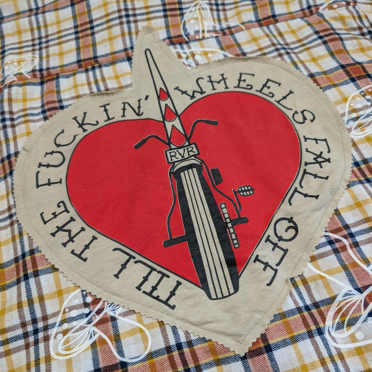 Heart-shaped sign with a bicycle graphic and text on a plaid fabric background