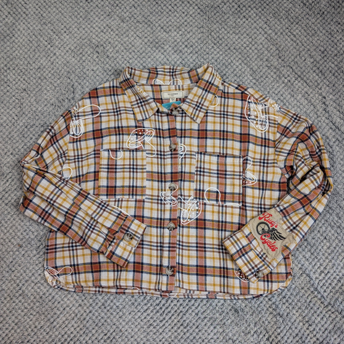 Plaid shirt with embroidered designs on a textured gray surface